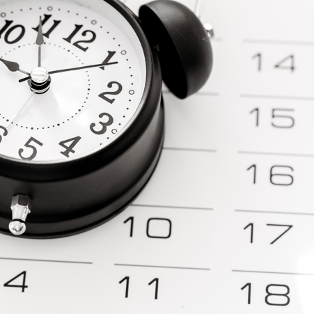 A black and white clock laying on top of a black and white calendar.